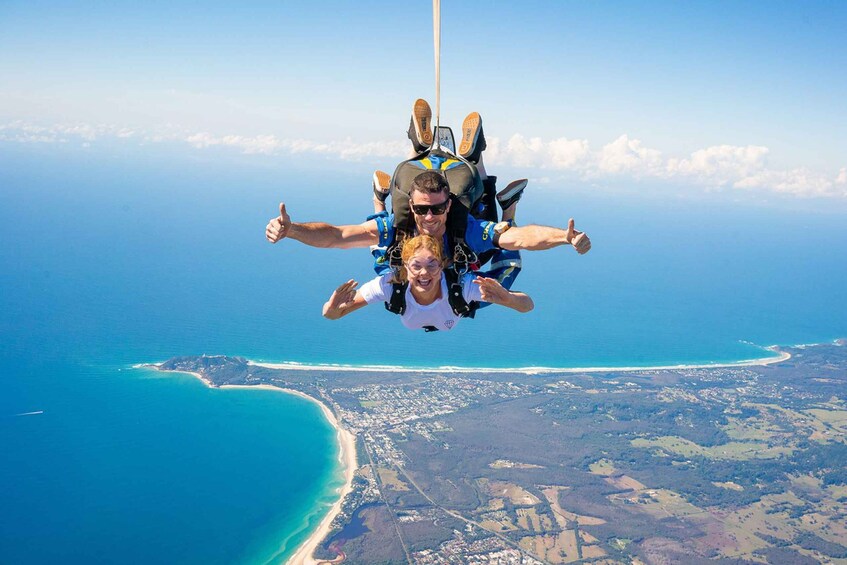 Two people skydiving with a parachute, overlooking a coastal landscape with a beach and urban area. 3