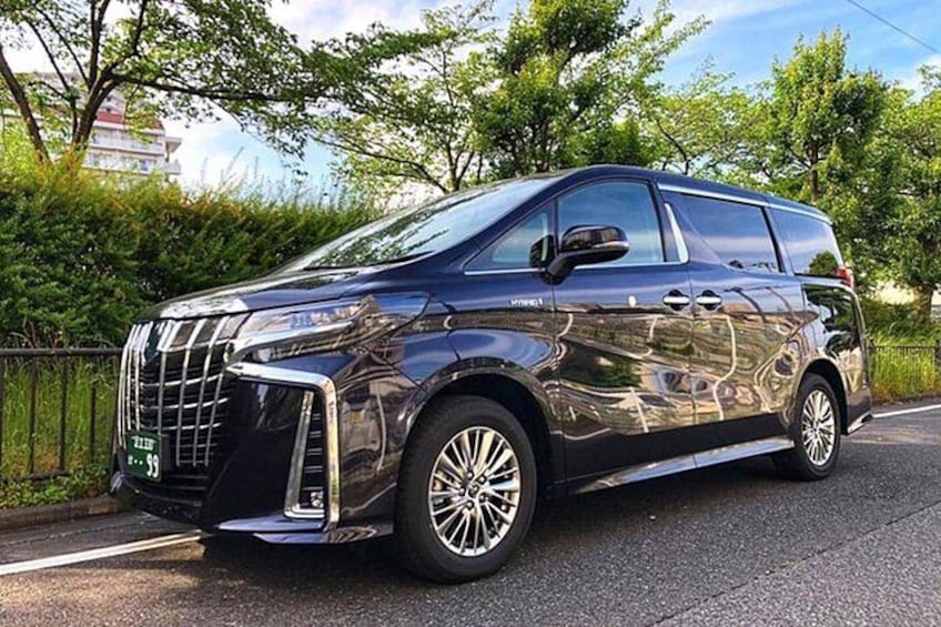 A dark-colored SUV parked on a road with trees and a fence in the background. 4