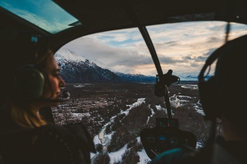 Ein Hubschrauber-Cockpit mit Blick auf eine verschneite Landschaft und Berge in der Ferne. 2