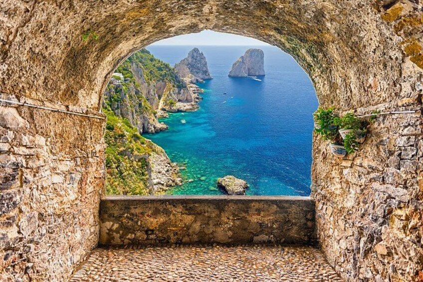 A stone archway overlooking a coastal landscape with clear blue waters and rocky cliffs. 2
