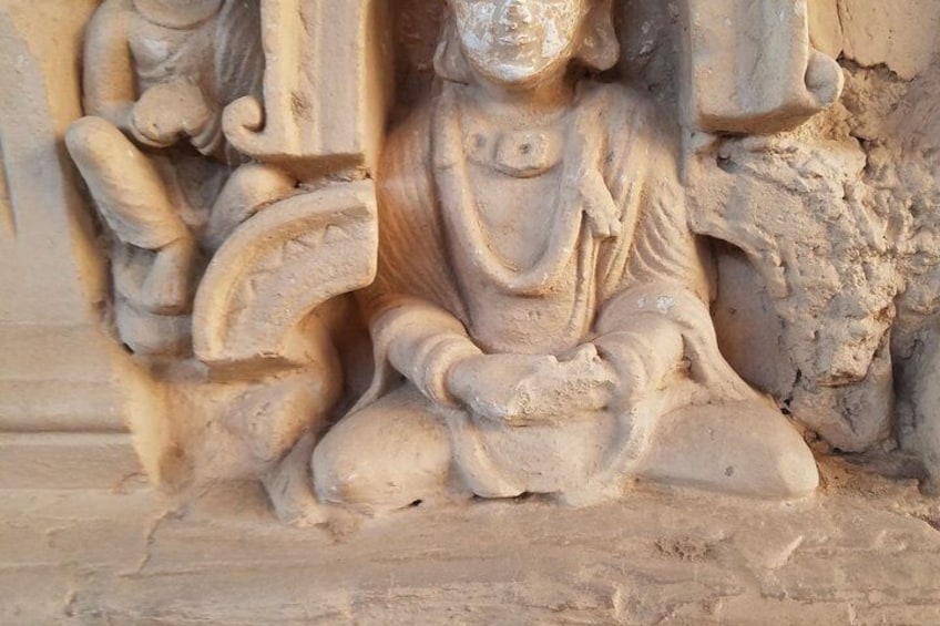 Une sculpture en pierre représentant une figure assise, les mains posées dans une attitude méditative, et entourée de sculptures complexes. 4