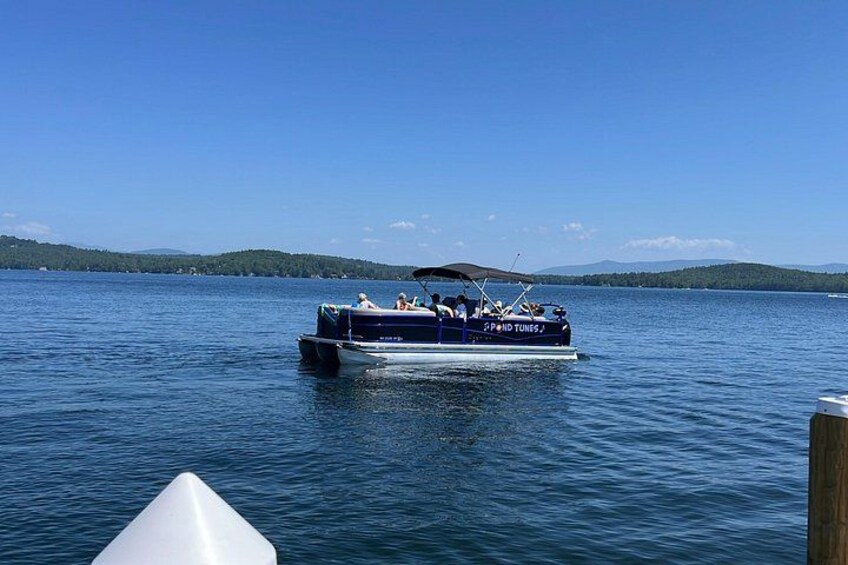 En båt med namnet ”SPOND TUNES” på en sjö, med klar himmel och avlägsna berg i bakgrunden. 2