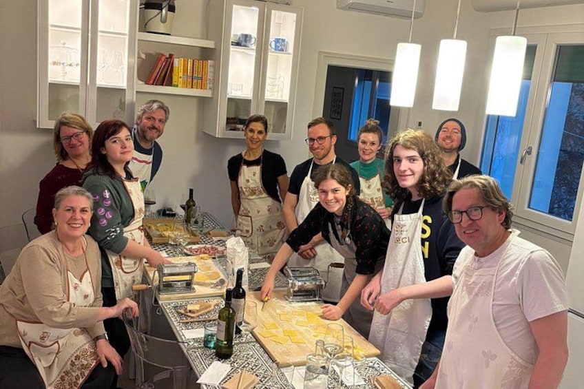 A group of people in a kitchen with a long table, cooking utensils, and ingredients. 1