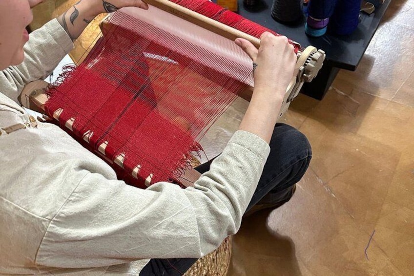 Una persona tejiendo con hilo rojo en un telar de madera. 1