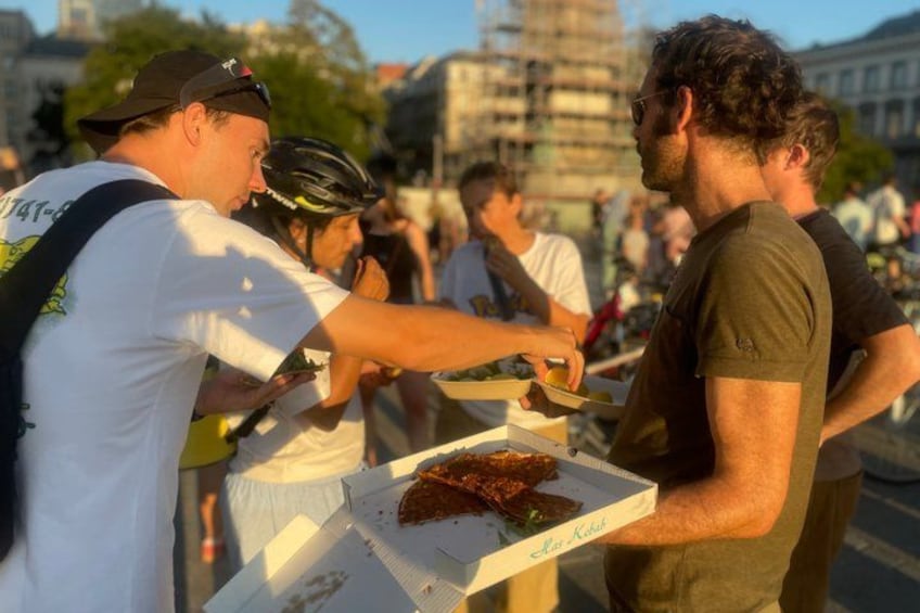 Des personnes se tiennent près d'un étal de nourriture, une boîte à pizza à la main. 1
