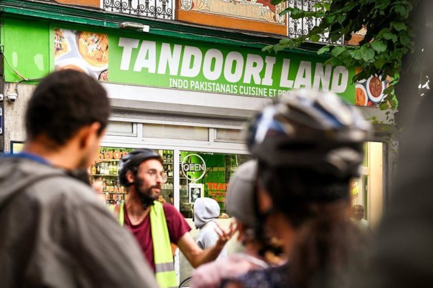 Une scène de rue avec un restaurant appelé « TANDOORI LAND » et un cycliste au premier plan. 2