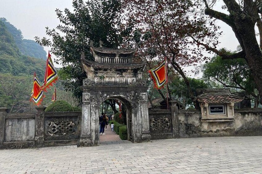 A traditional gate with flags, a paved pathway, and a mountainous backdrop. 2