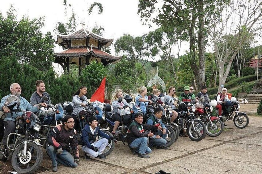 A group of people sitting on motorcycles in a park with a pagoda in the background. 4