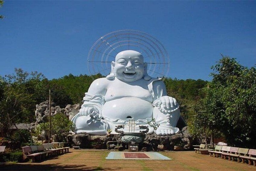 A large white Buddha statue with a smiling face, surrounded by a grassy area with benches and trees. 2