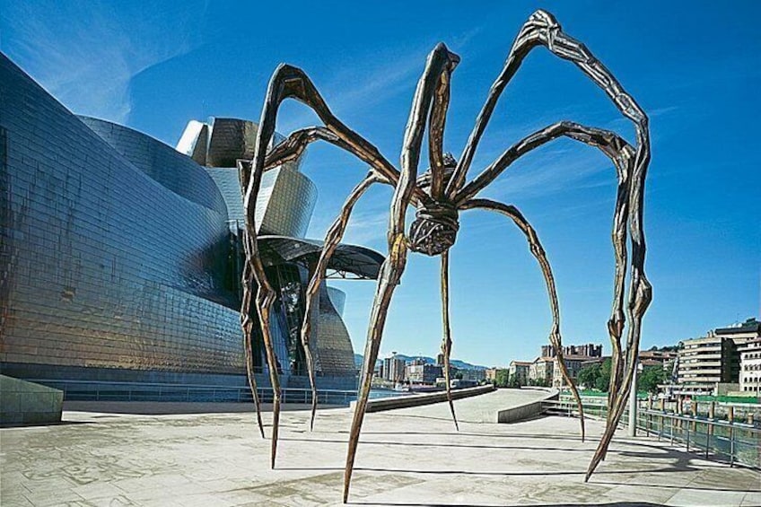 En stor metalskulptur af en edderkop i et bymiljø med moderne arkitektur i baggrunden. 5