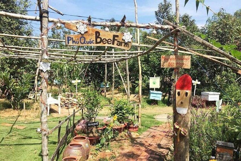 A rustic beekeeping setup with a sign reading 'Phu Quoc Bee Farm,' beehives, and a wooden structure. 2