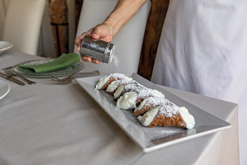 A person sprinkling powdered sugar over a dessert on a white plate. 2