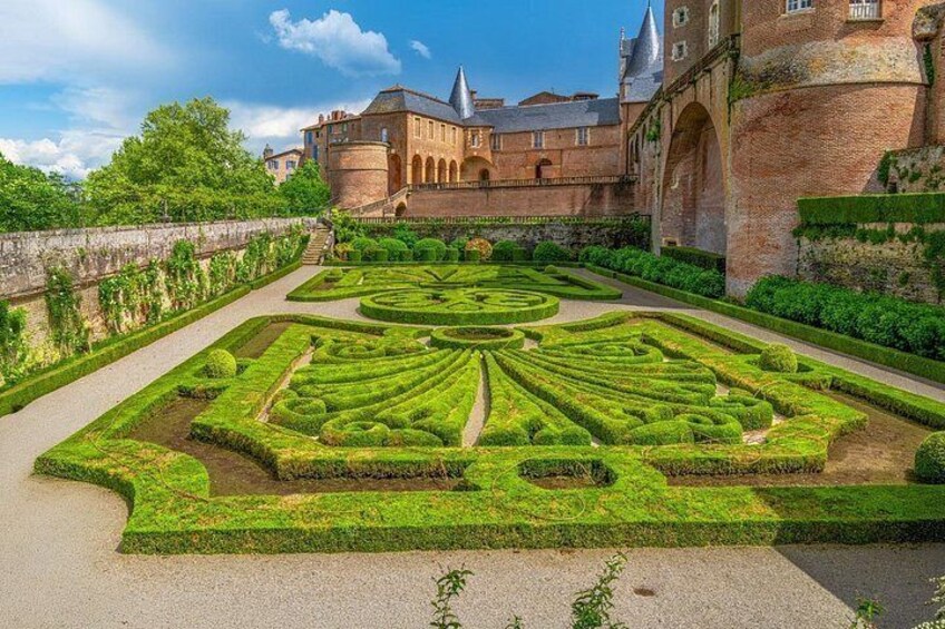 Ein formaler Garten mit geometrischen Mustern, ein großes Backsteinhaus und ein klarer Himmel. 4