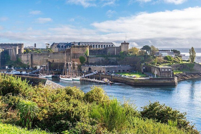 Un pueblo costero con una fortaleza histórica, un puerto con barcos y abundante vegetación. 4