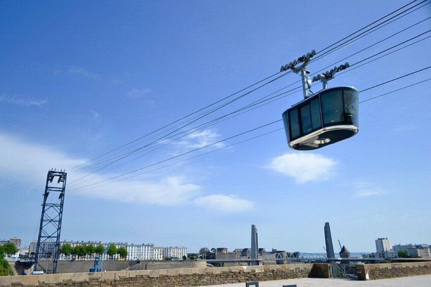 Un teleférico suspendido por cables contra un cielo despejado, con edificios y un puente al fondo. 3