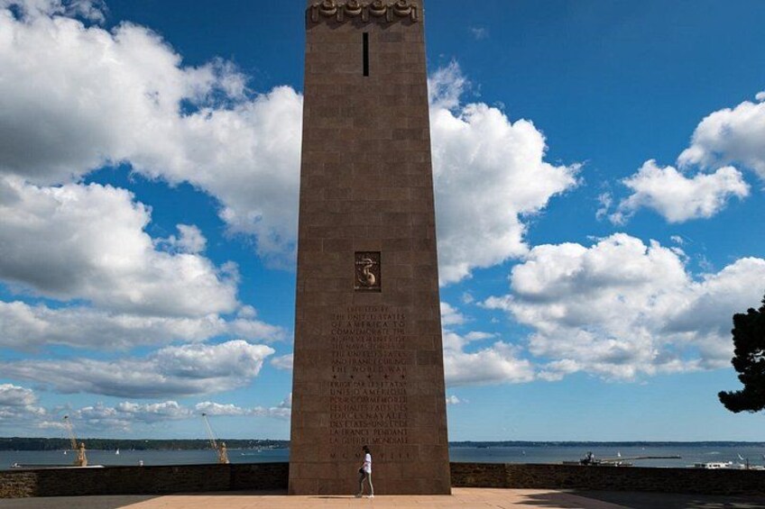 Un monumento alto con inscripciones, un cielo despejado y una vista distante del océano. 2