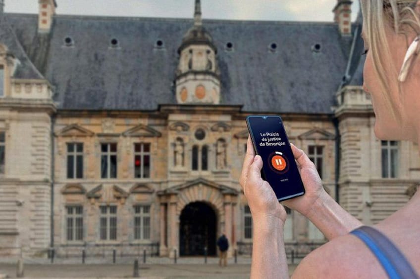 A person holding a smartphone with an app interface in front of a historic building. 2