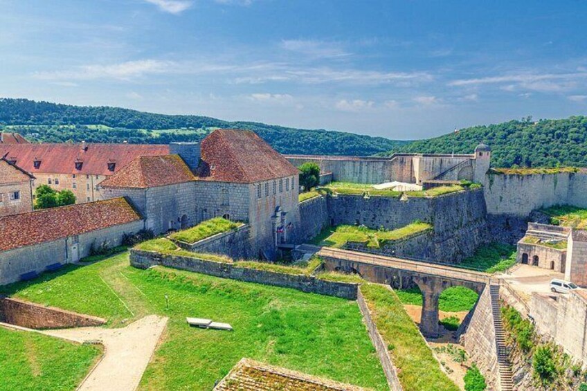 A historic fort with stone walls, a grassy courtyard, and a bridge. 2