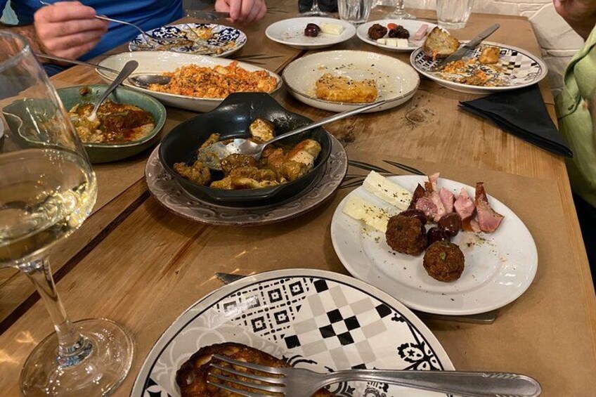 Una mesa de comedor con diversos platos, incluyendo un plato con carne y verduras, un bol con salsa oscura y una copa de vino blanco. 2