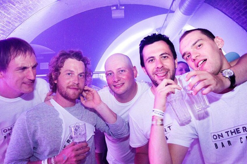 A group of people in a bar setting with a curved ceiling and purple lighting. 4