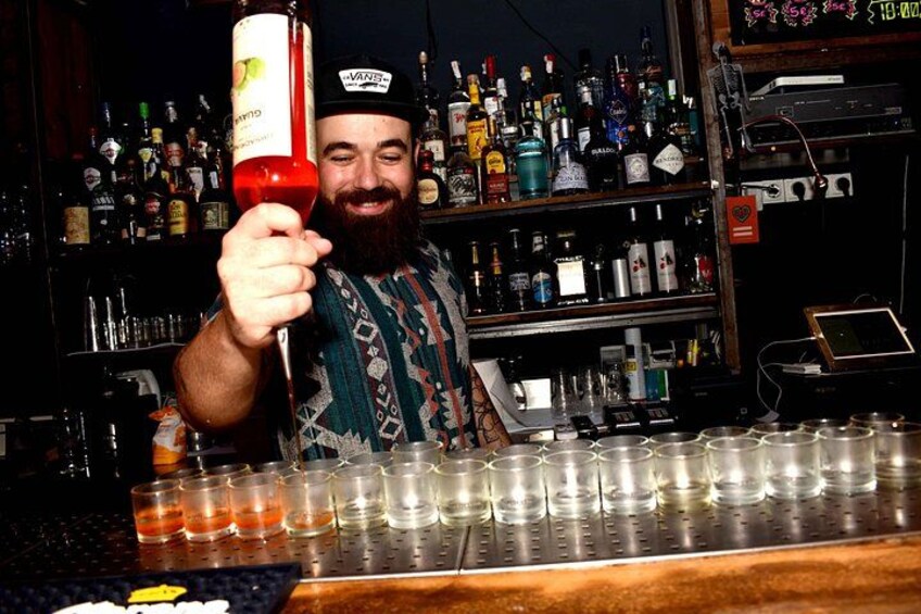 A person holding a bottle, a bar counter with shot glasses, and shelves with bottles in the background. 5