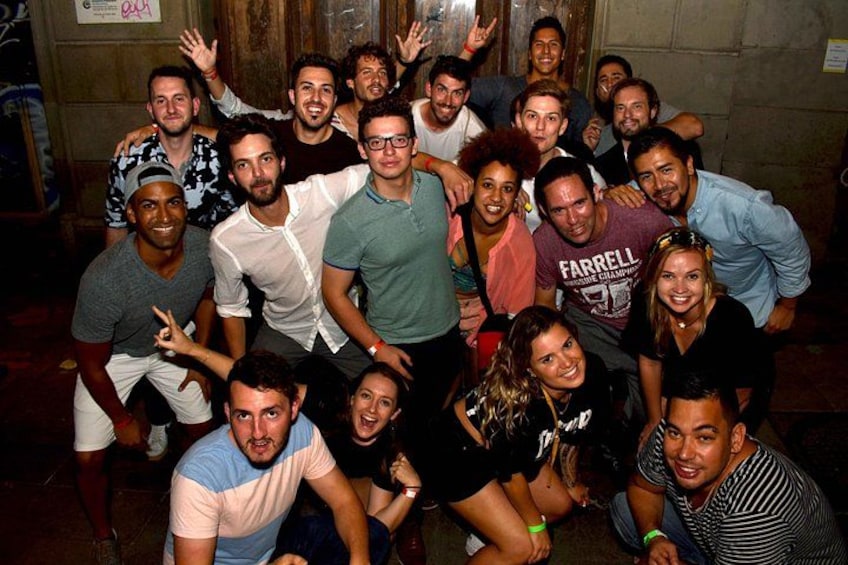 A group of people posing together in an indoor setting with wooden walls and a door in the background. 1