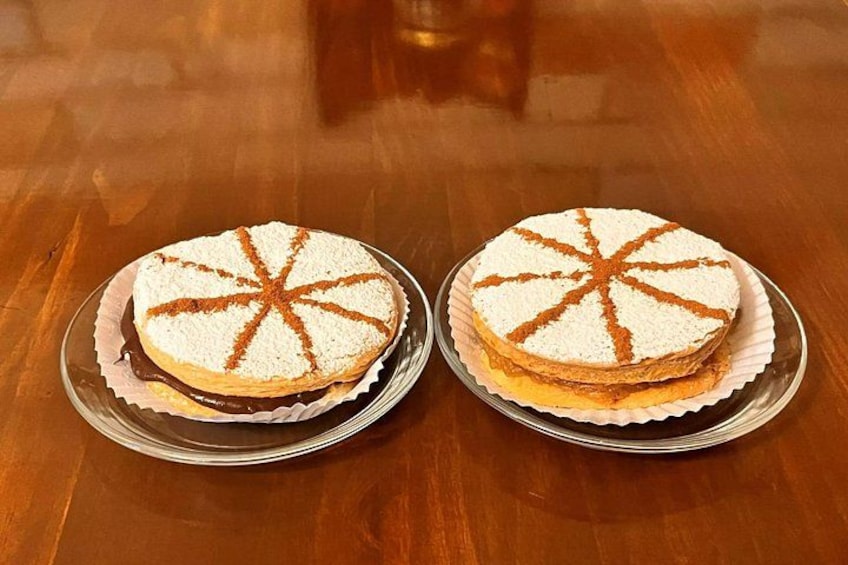 Two round cakes with white frosting and brown designs on a wooden table. 1