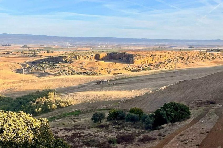 A vast, arid landscape with rolling hills, sparse vegetation, and a clear sky. 2
