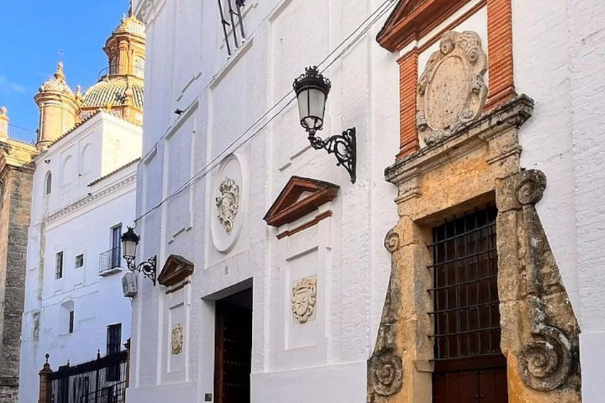 A white building with ornate wooden window frames, a black wall-mounted lamp, and a decorative stone plaque. 3