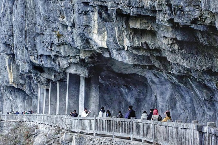 Une falaise rocheuse avec une passerelle en bois, et des personnes qui observent le paysage. 5