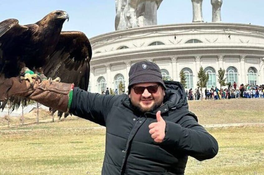 Une personne porte un tatouage d’aigle sur le bras et se tient devant un grand bâtiment blanc orné de colonnes. 1