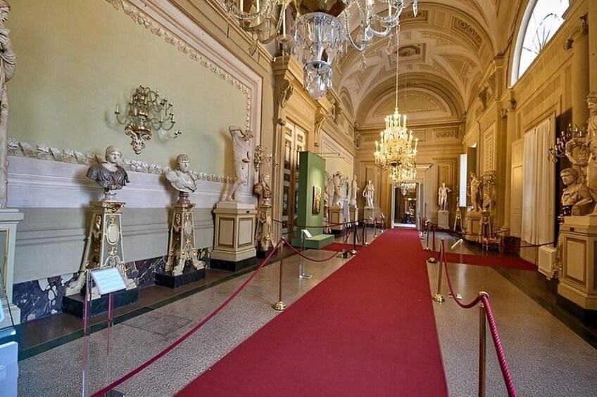 A grand hallway with a red carpet, ornate chandeliers, and classical statues. 4