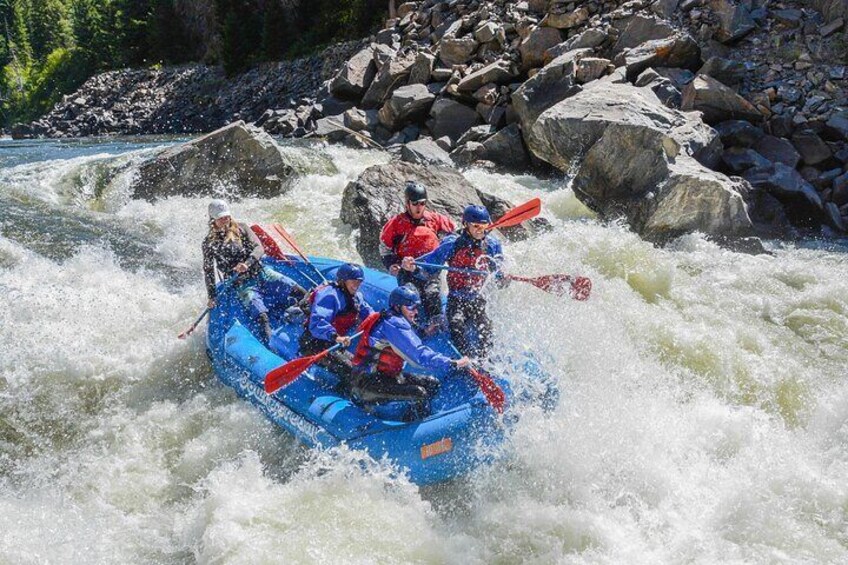 A group of people in a blue raft navigating a river with rapids. 1