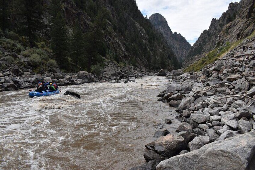 A river with a raft carrying people, surrounded by rocky terrain and dense forest. 4