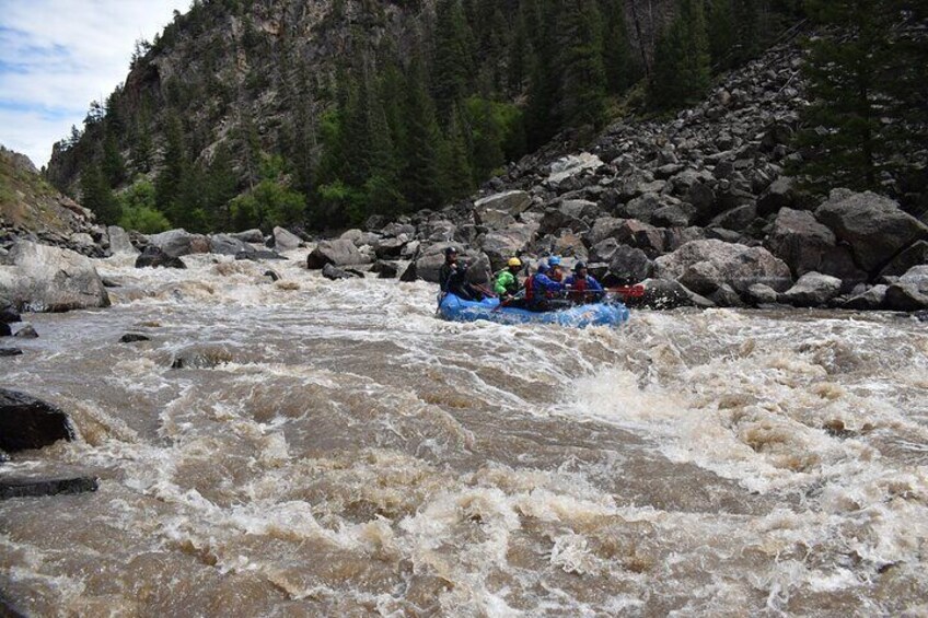 A group of people rafting down a turbulent river surrounded by rocky terrain and dense forest. 5