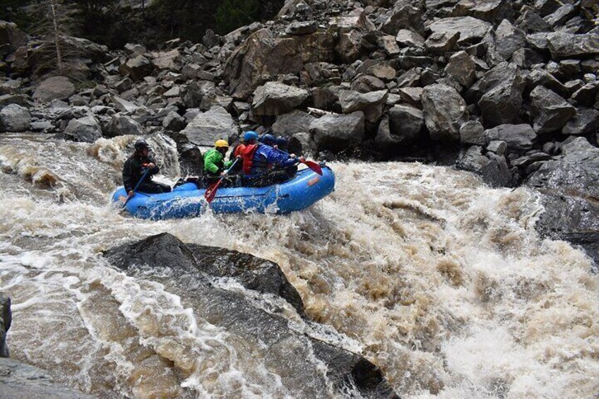 A blue raft navigating turbulent rapids with large rocks. 3