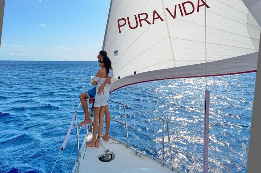 A sailboat with the text 'PURA VIDA' on its sail, two people on the deck, and the ocean in the background. 3