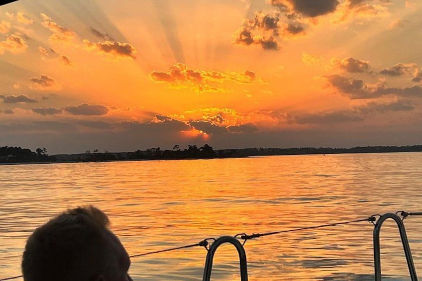 A sunset over a body of water with a silhouette of a person and a boat's railing in the foreground. 4