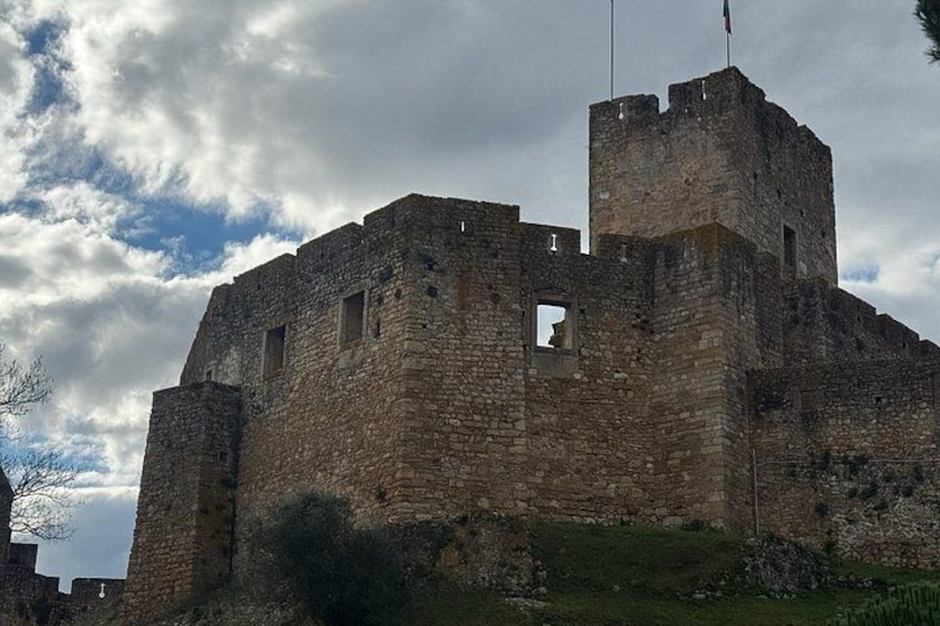 Un château de pierre historique, doté de créneaux, d’un mât pour drapeau et surplombant un ciel nuageux. 3