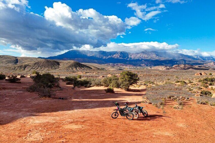 A desert landscape with a mountain range in the background and a motorcycle parked on the ground. 1