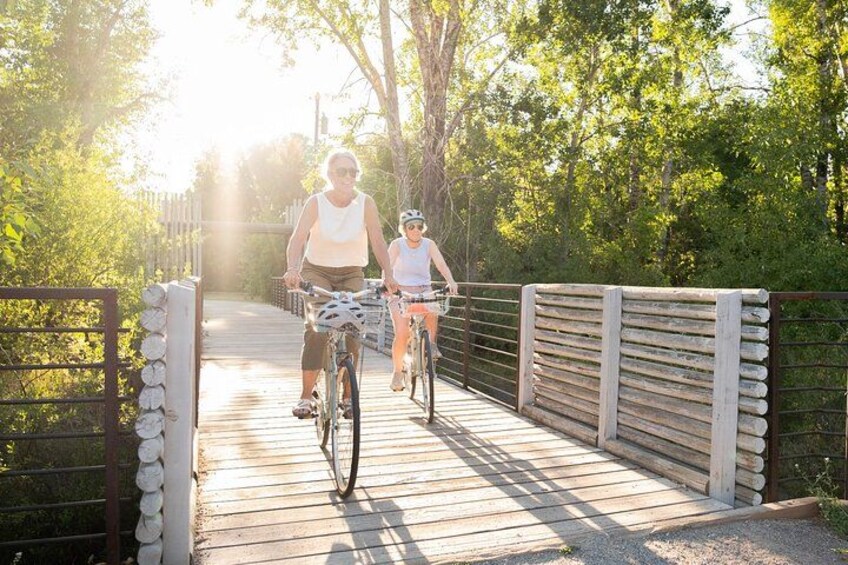 Deux personnes à vélo traversent un pont en bois, entouré de verdure. 3