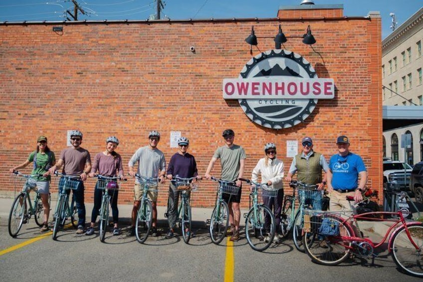 A group of cyclists in front of a brick wall with a cycling logo. 5