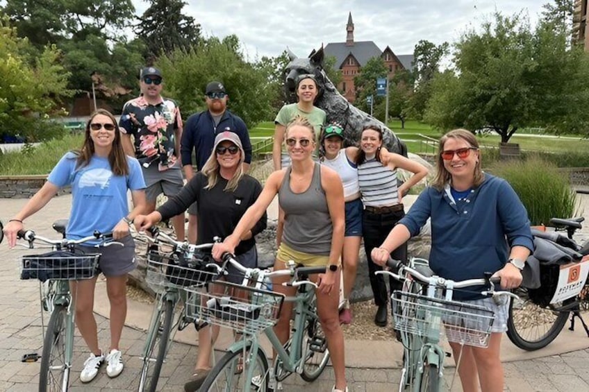 A group of people with bicycles in a park with a statue and a building in the background. 2