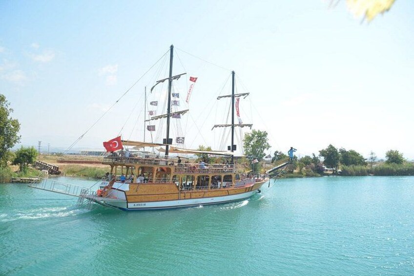 A traditional wooden boat with multiple masts and flags, sailing on a calm body of water. 2