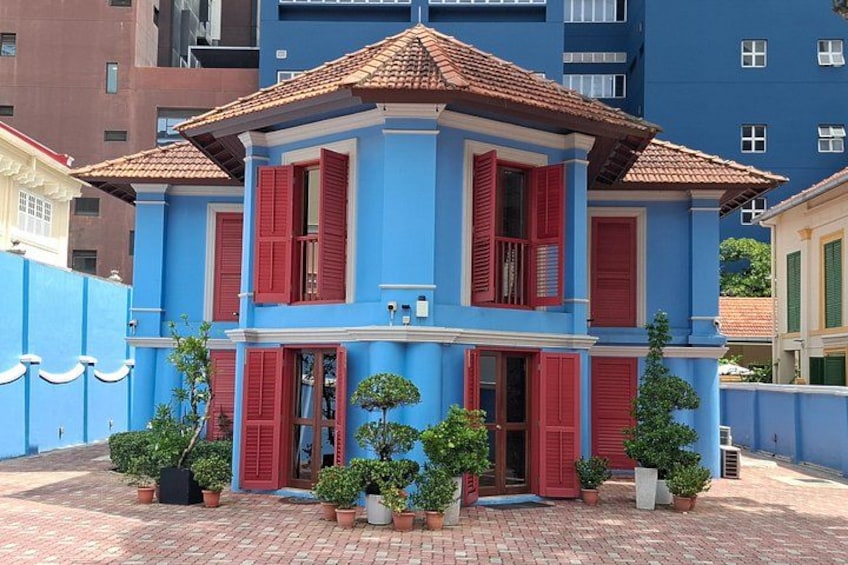 Ein blaues Haus mit roten Fensterläden, umgeben von Topfpflanzen und einem Ziegelweg. 3