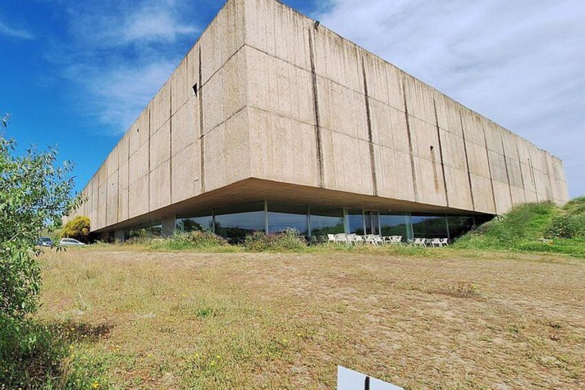 Un grand bâtiment en béton doté d’un toit plat, avec un champ verdoyant au premier plan. 1