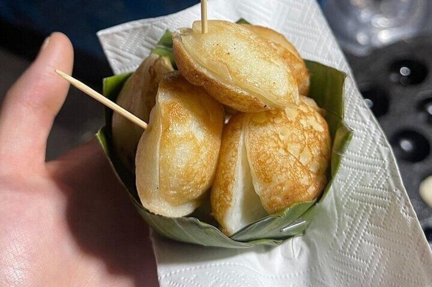 Una mano sostiene una cesta con bolitas de masa frita doradas y palillos. 4