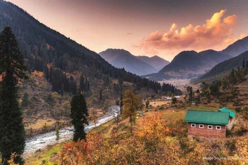 A mountainous landscape with a river, a small building with a green roof, and autumn-colored trees. 5