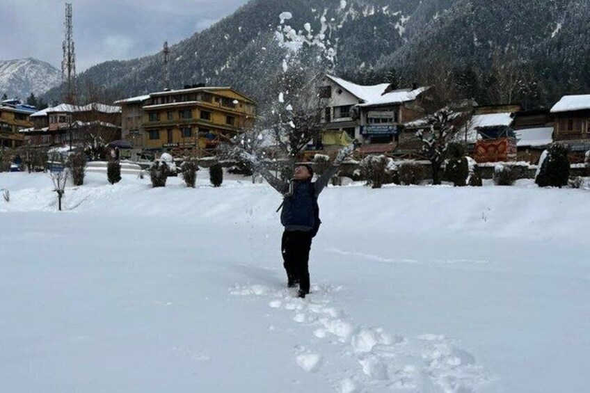 A person playing in the snow with footprints in the background and buildings in the distance. 2