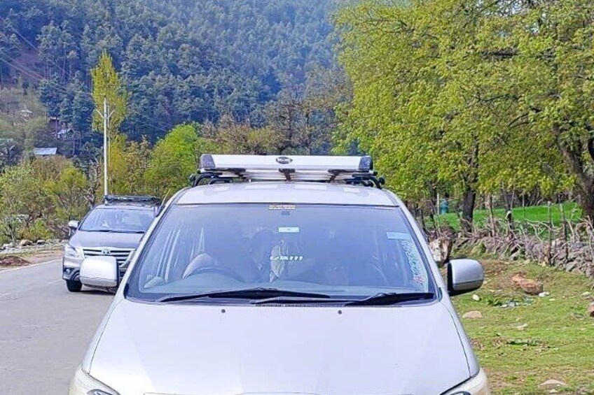 A silver car with a roof rack parked on a road with a mountainous background. 4